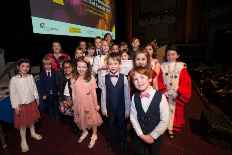 Young children looking smart stand on a stage smiling at the camera