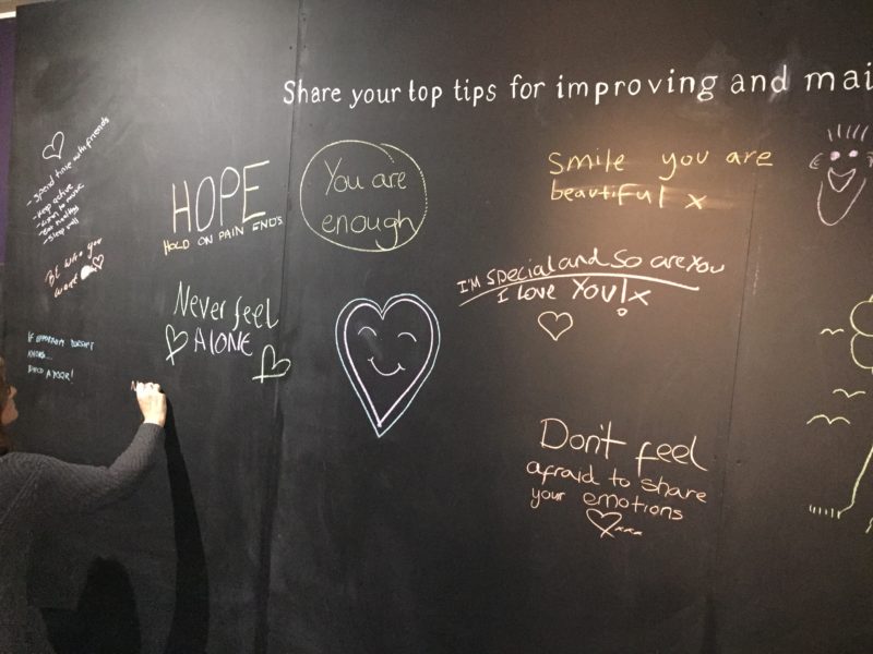 Blackboard with someone writing on it in chalk. It says You are enough, never feel alone, i love you, don't feel afraid to share your emotions.