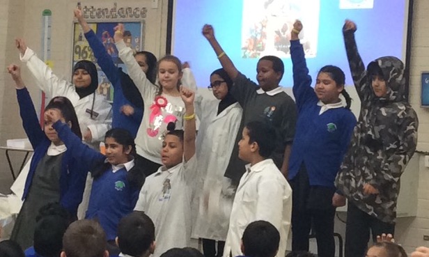 Group of young children in school uniforms with their hands up to answer questions