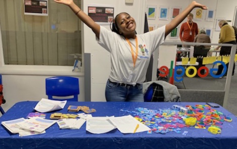 Young person stood with arms in the air, excited, in front of table of work