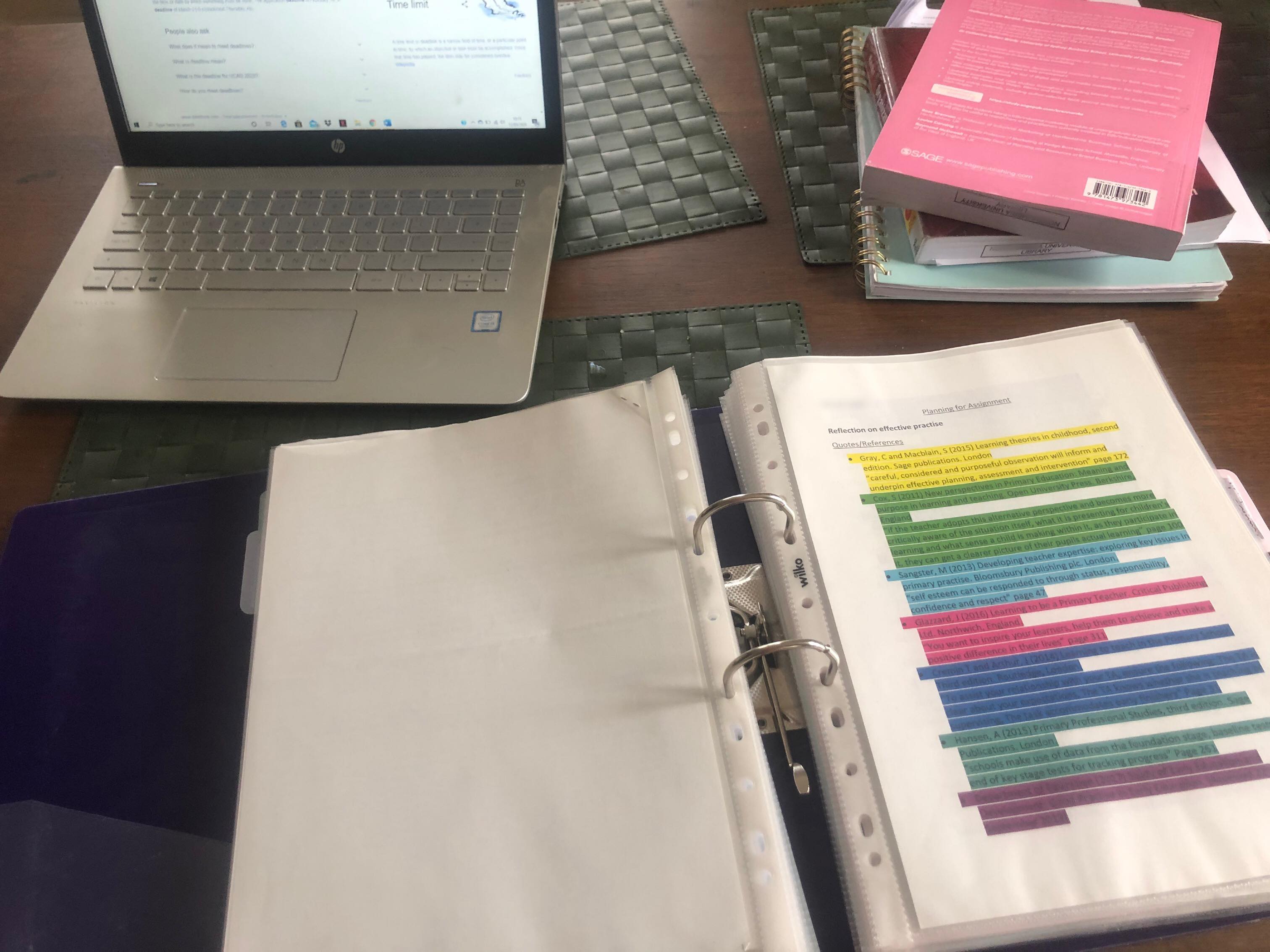 Desk with laptop, folders of work and a stack of books